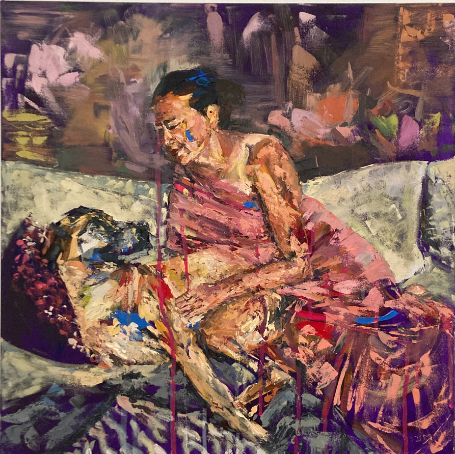 A woman wearing a pink saree sits on a sofa next to a large tan and black dog who looks back at her. Her hand rests on his foreleg and she looks down at him.